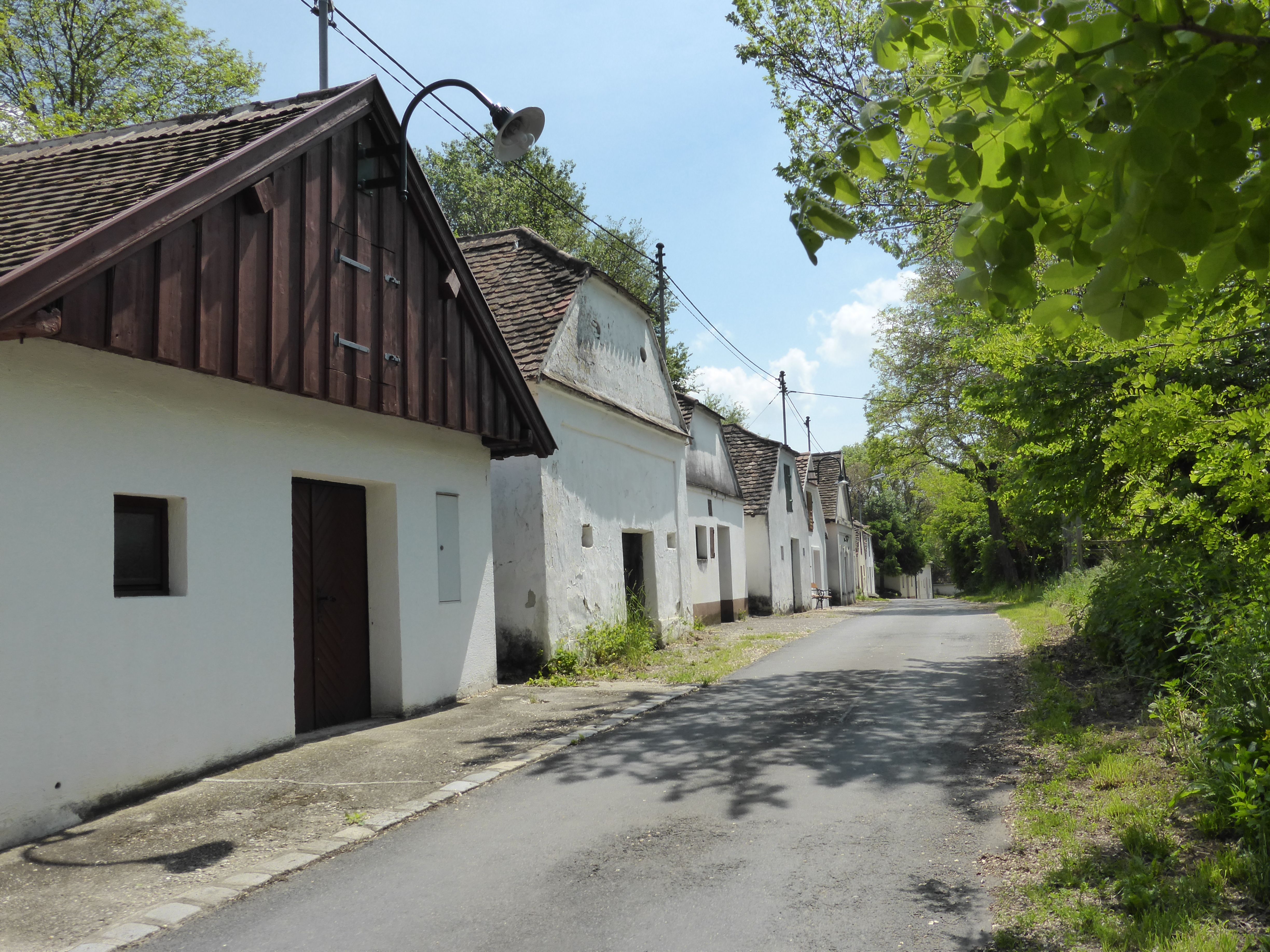 Row of traditional white houses along a quiet street, surrounded by trees and green foliage.