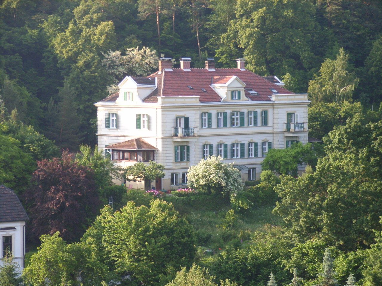 Large, white building surrounded by greenery and trees.