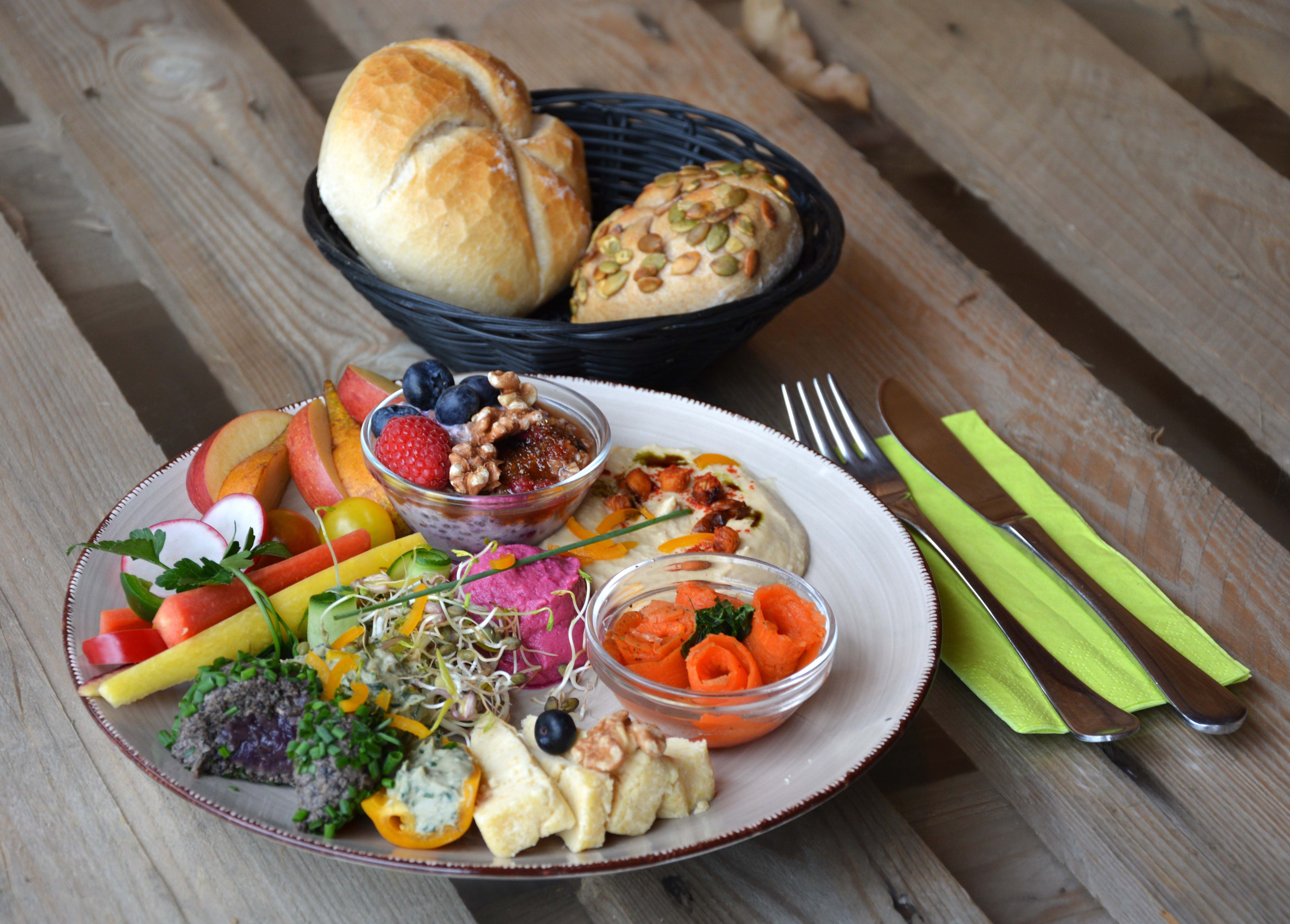 Colorful breakfast plate with hummus, cheese and vegetables, next to cutlery and a bread basket.