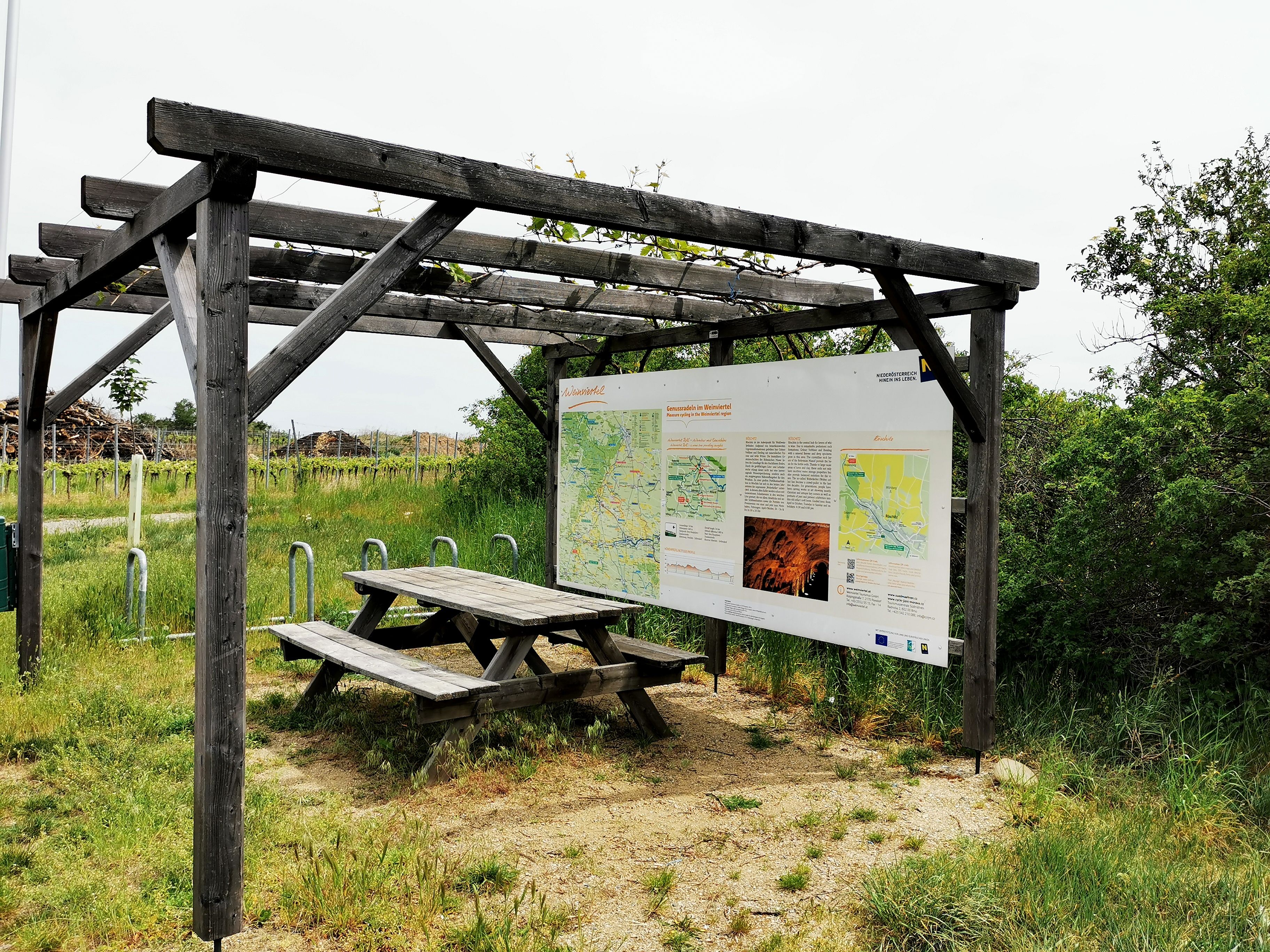 Wooden pergola with information board and picnic table in a rural setting.