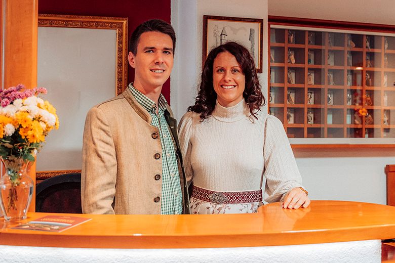 A man and a woman stand smiling behind a reception counter in traditional dress.