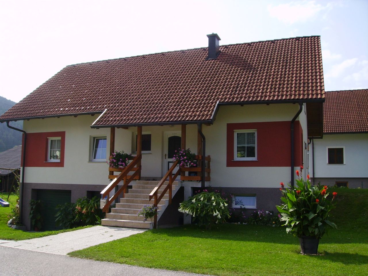 A detached house with a red roof and white and red façade, surrounded by a well-tended garden and flowers.