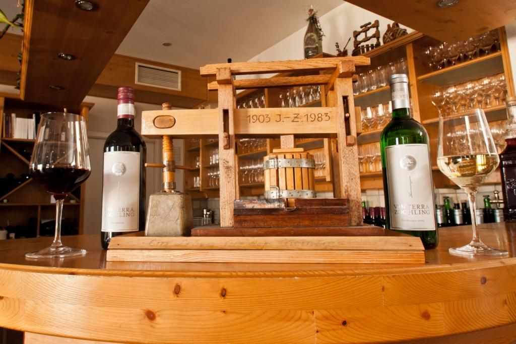 Wine bottles and glasses next to a small wooden press on a counter.