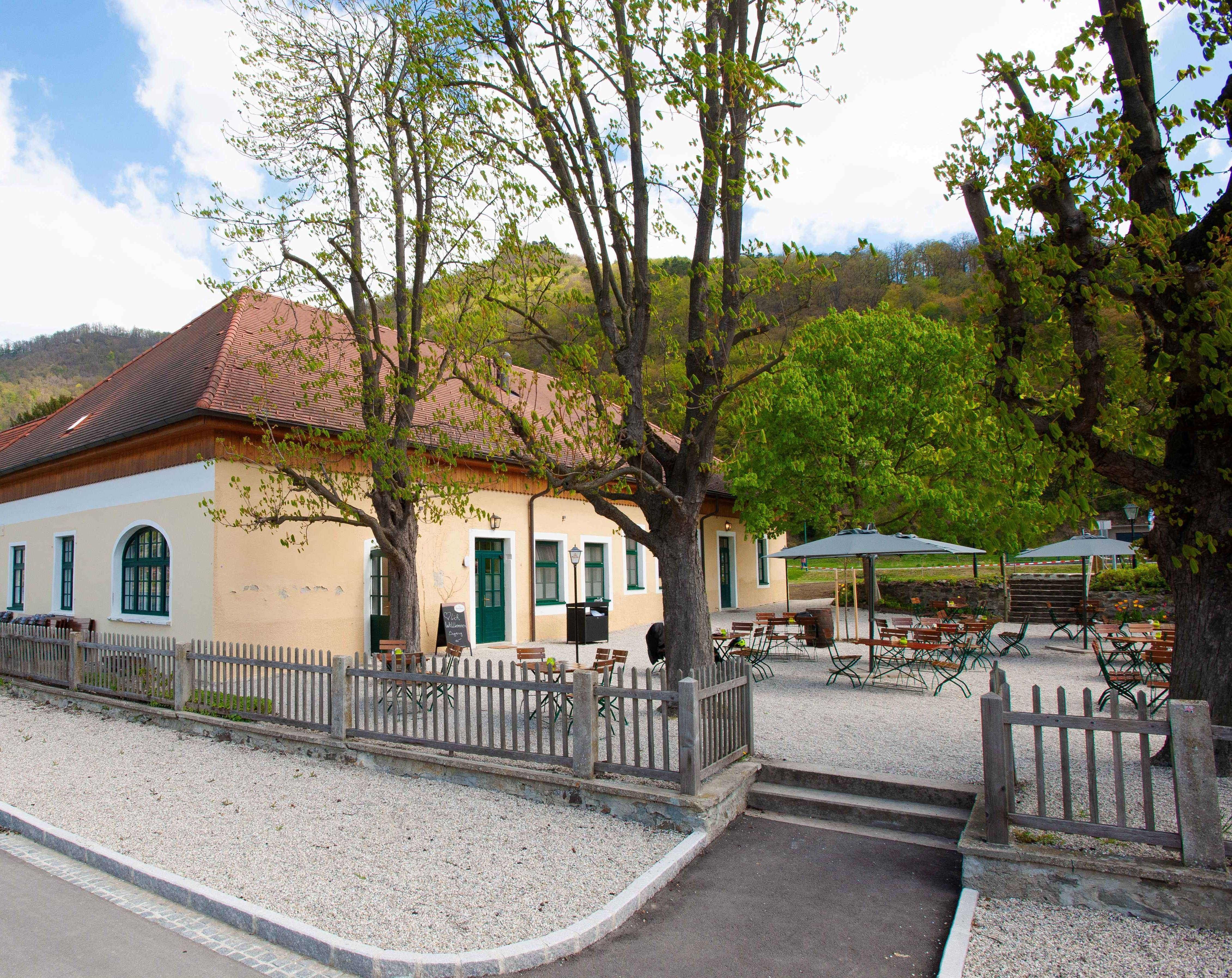 Exterior view of a yellow building with a red roof and beer garden.