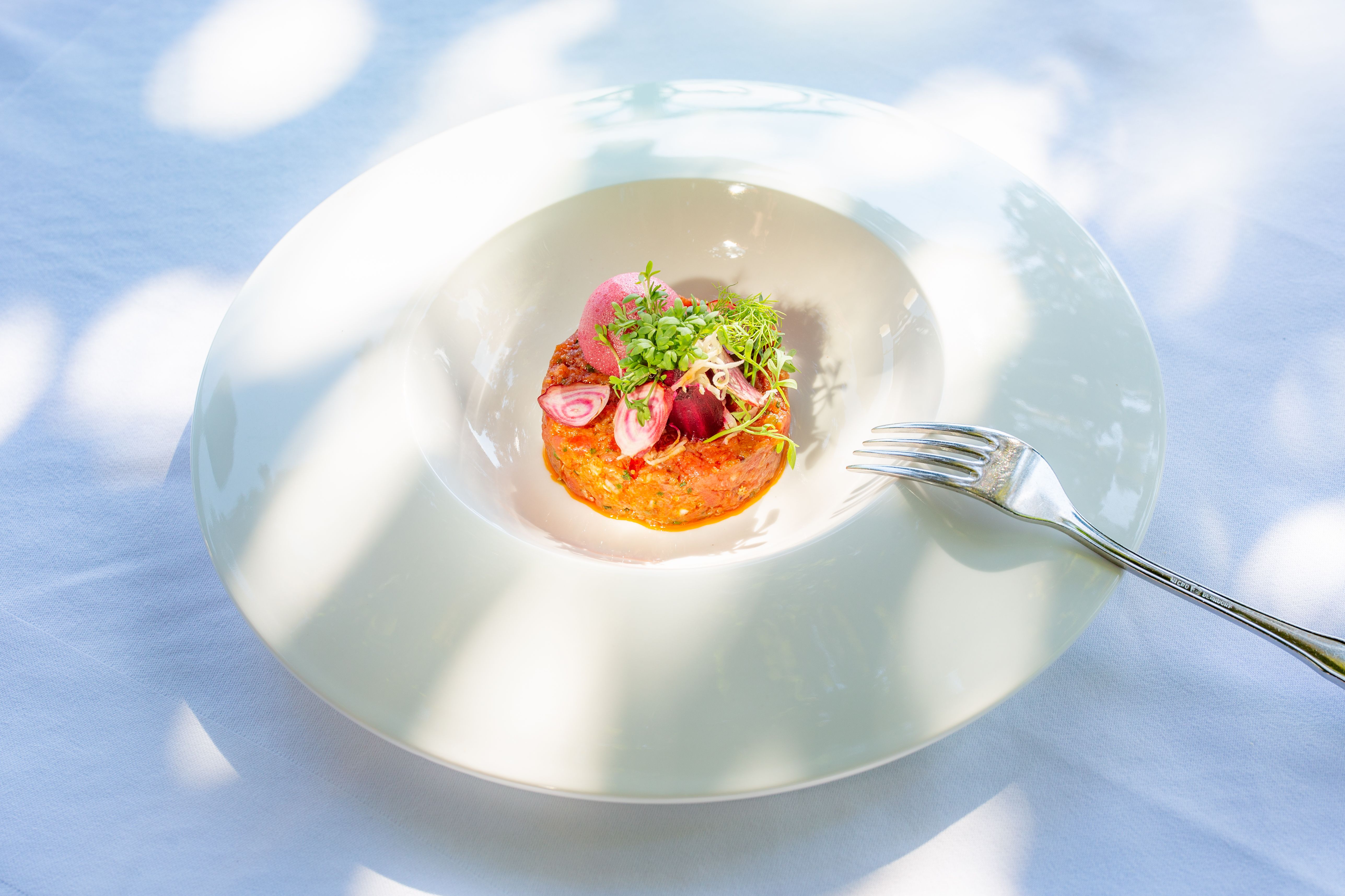 An artfully arranged dish on a white plate with a fork next to it.