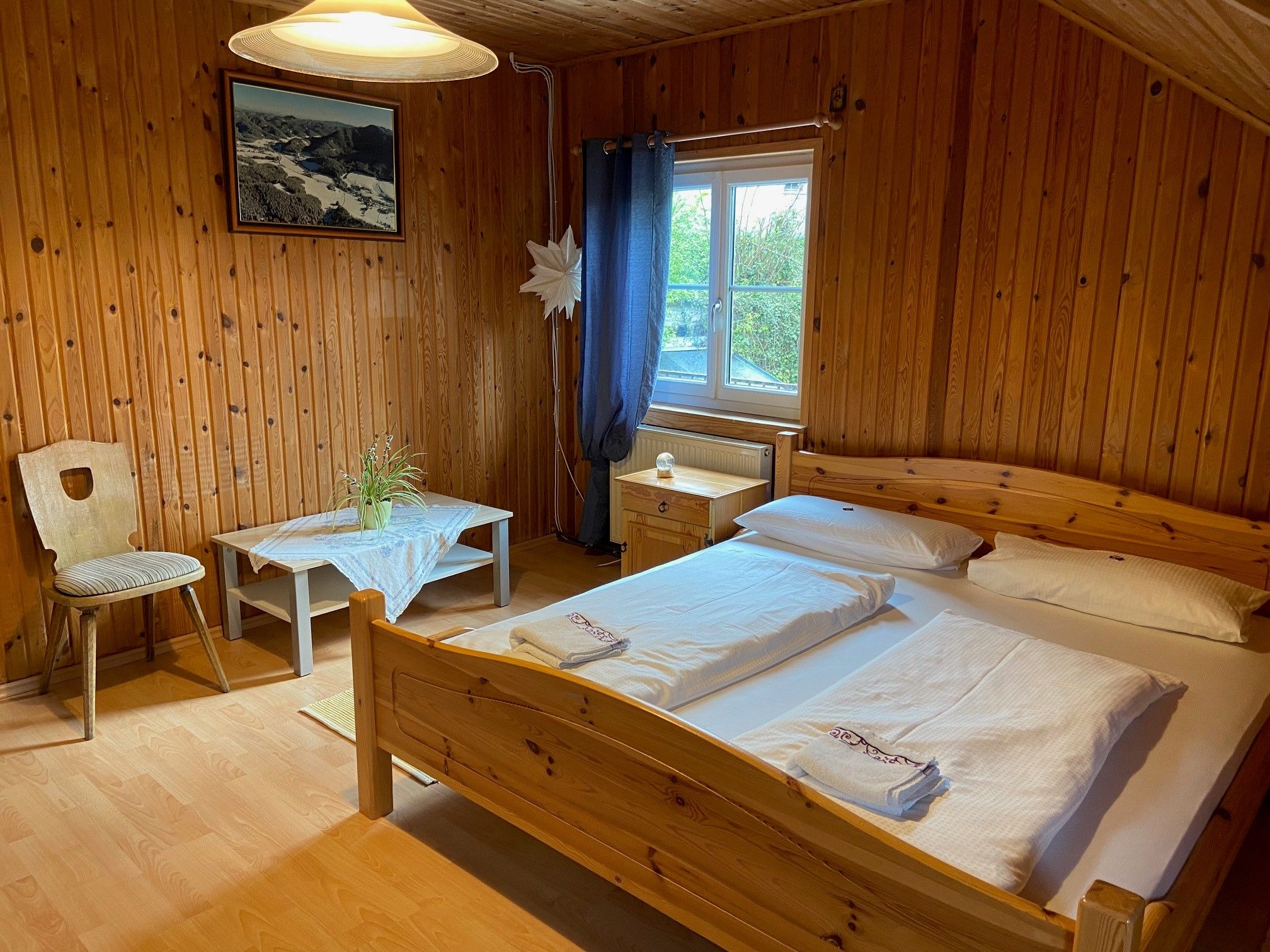 Wood-paneled double room with bed, table, chair and window.