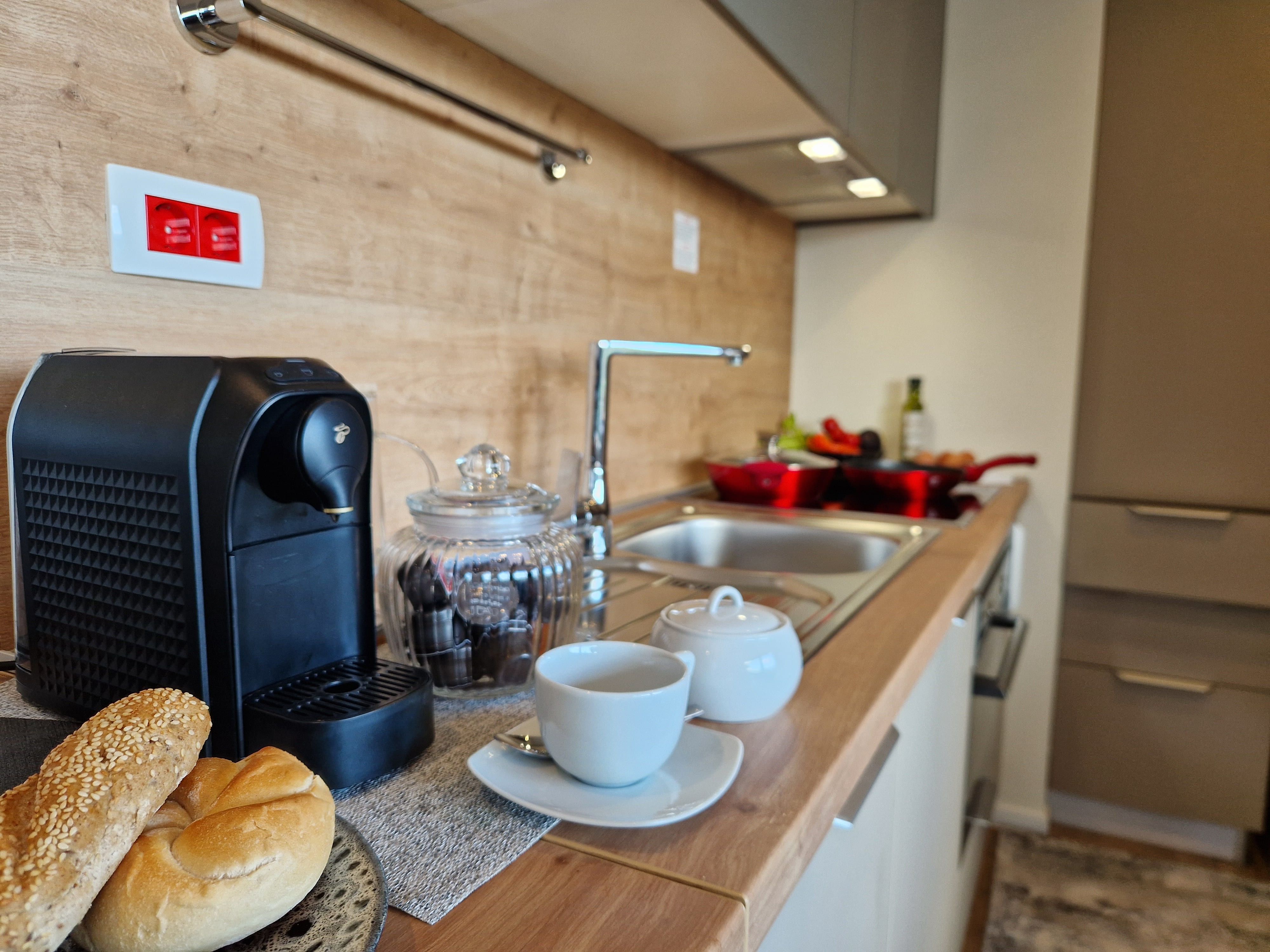 Modern kitchen with coffee machine, bread rolls and crockery on the worktop.