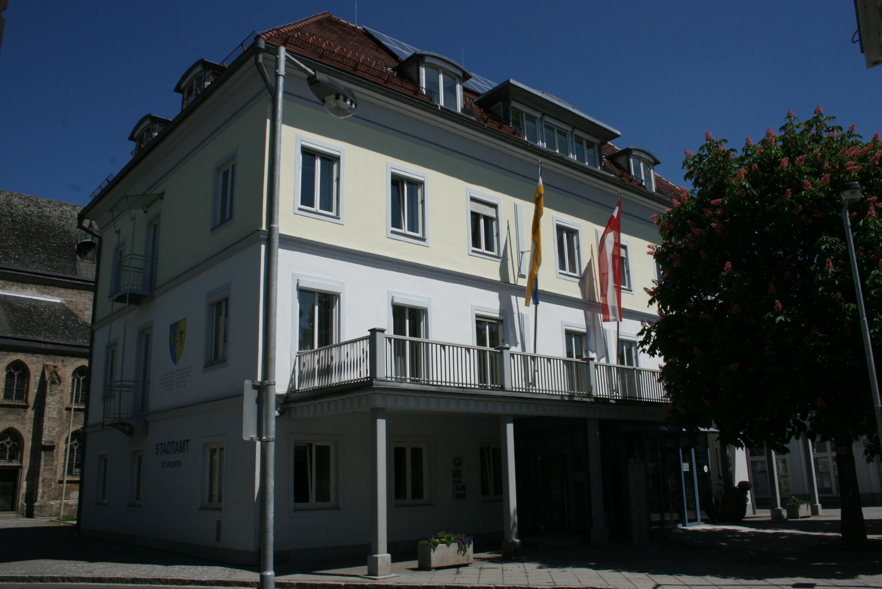 Building of the St. Valentin municipal office with flags and tree in the foreground.