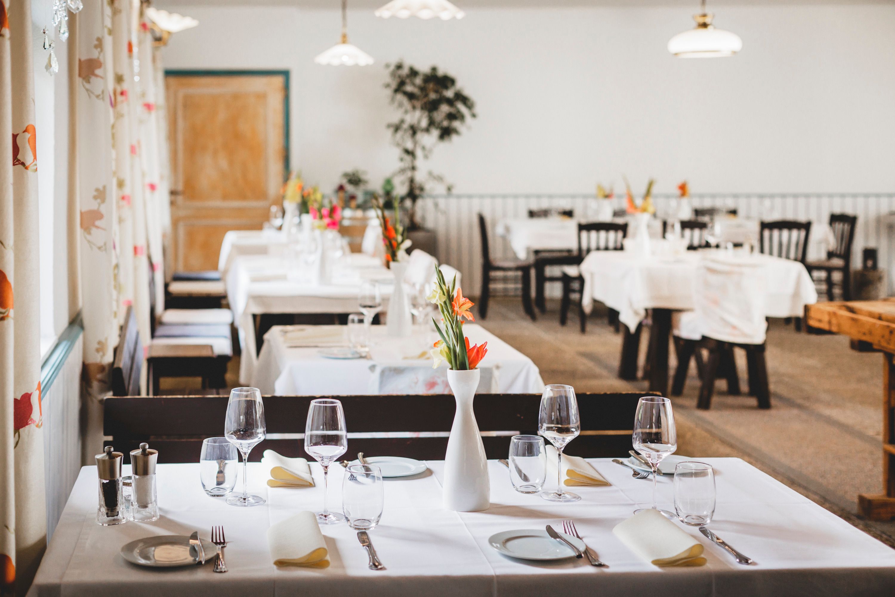 Elegant restaurant with white-clothed tables and flower vases.