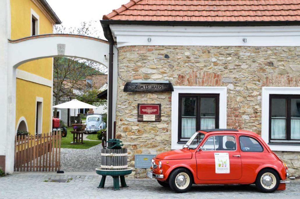 Entrance to a wine tavern with a red vintage car and a yellow building.