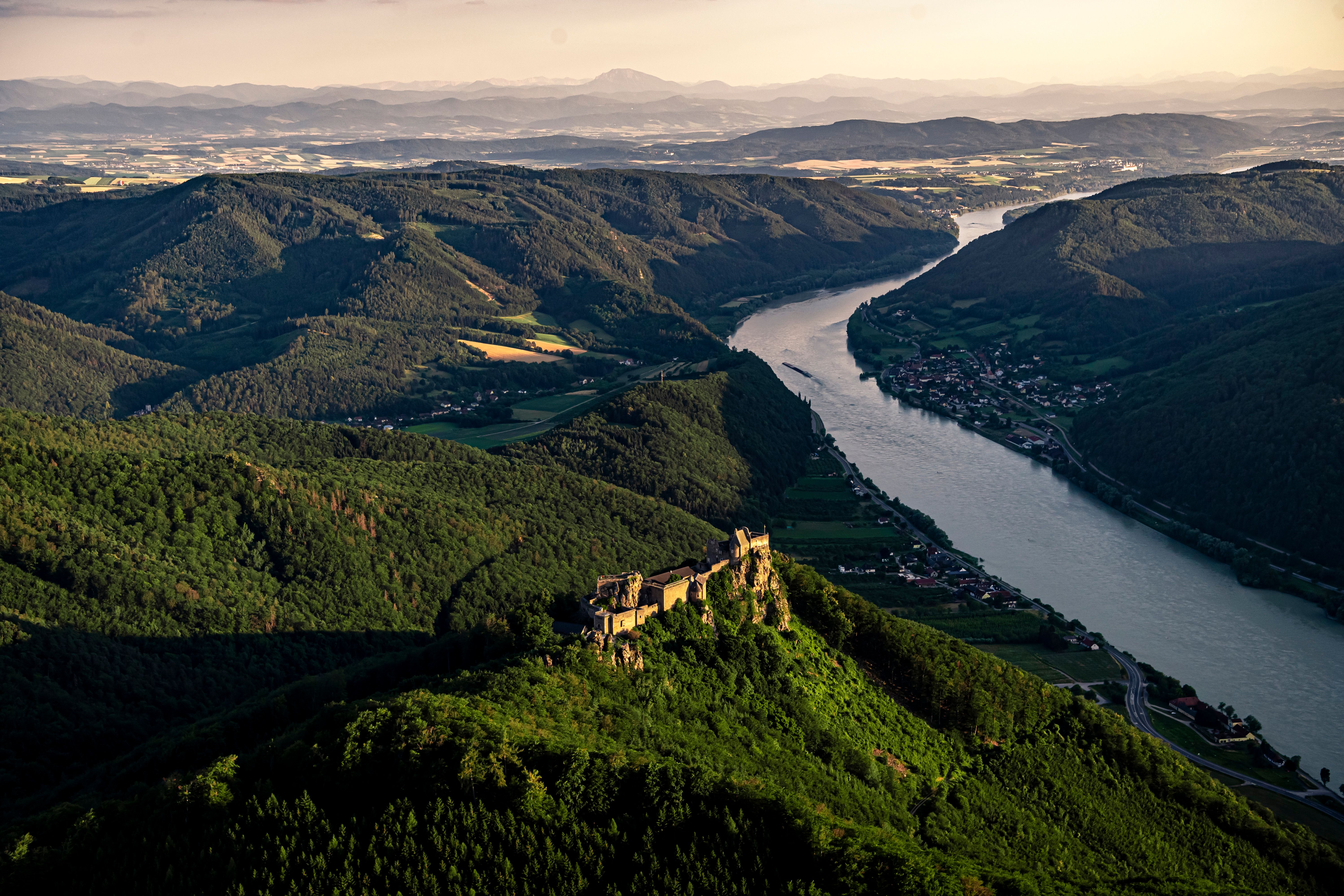 A hiker with a rucksack looks at the ruins of Aggstein Castle on a sunny day.