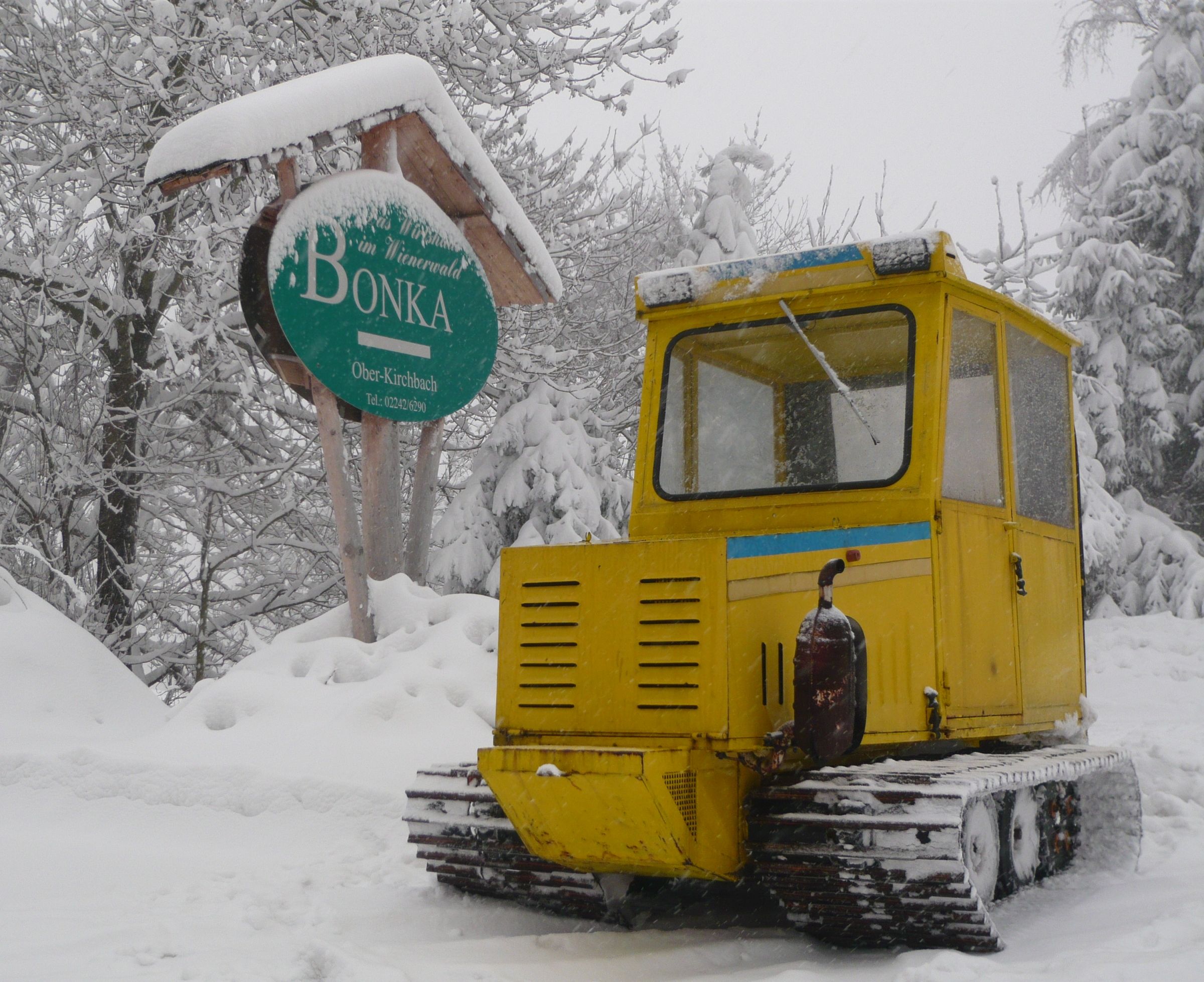 Yellow snow vehicle in the snow in front of a sign with the inscription 'Bonka' in Oberkirchbach.