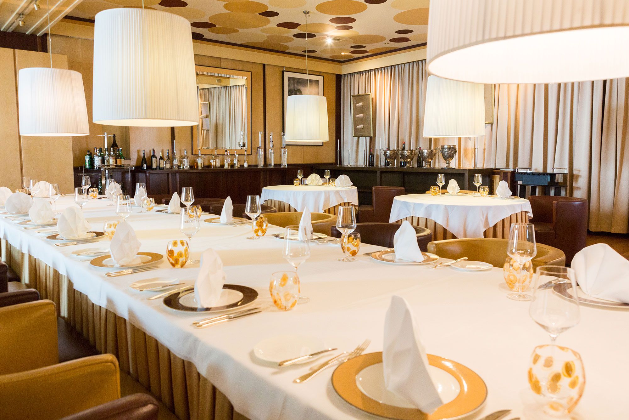 Elegant dining room with laid tables, white tablecloths and large hanging lamps.