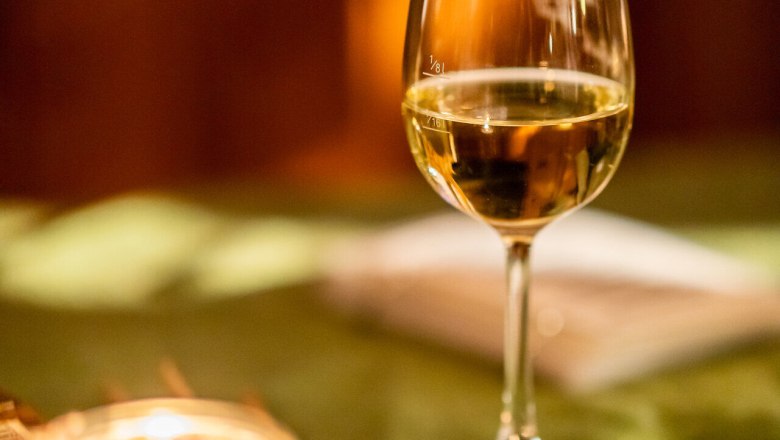 A glass of white wine with a candle on a table with a green tablecloth.