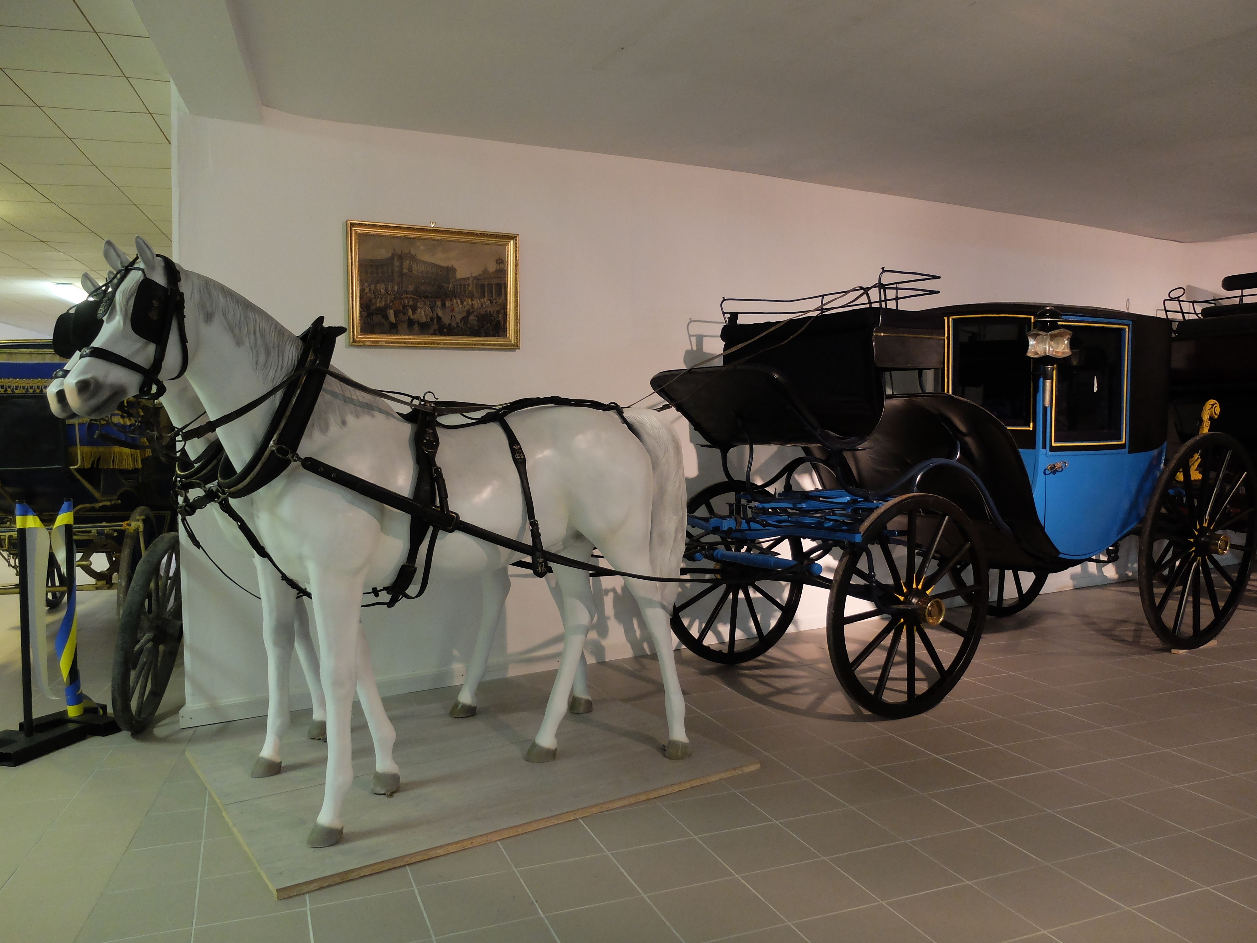 A historic carriage with a white horse model in a museum.