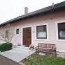 Entrance to a pink-painted vacation apartment with a wooden door, two windows and a wooden bench next to it.