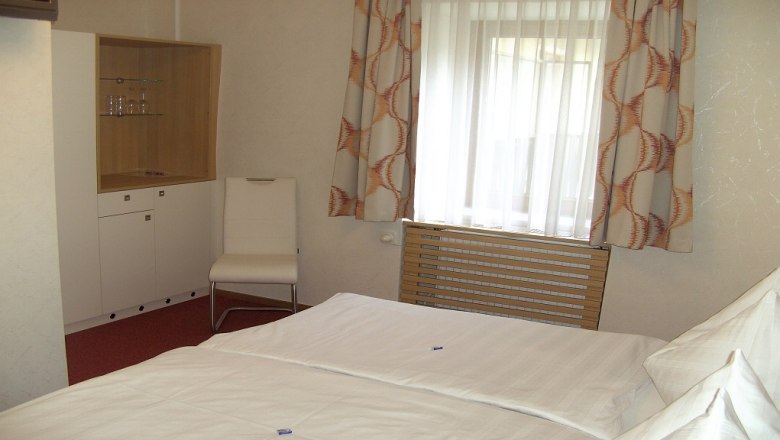 A hotel room with a bed, a chair, a wardrobe and a window with curtains.