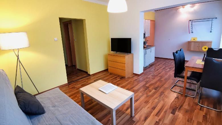 Modern living room with wooden floor, sofa, table, TV and dining area.