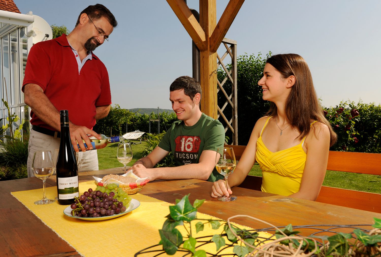 A man pours wine for two people at an outdoor table.