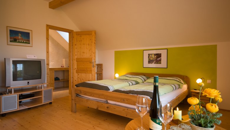 Cozy room with double bed, TV, bottle of wine and flowers on the table.