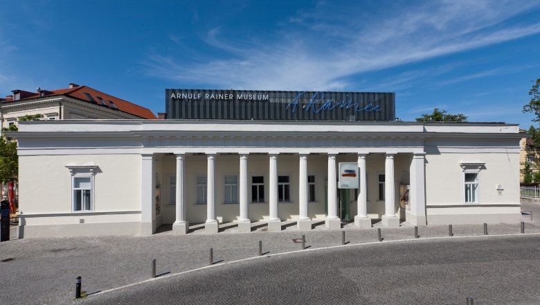 Exterior view of the Arnulf Rainer Museum with columned façade and blue sky.