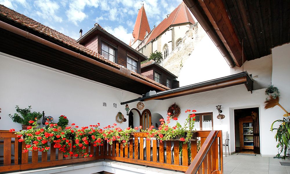 A terrace with red flowers, a wooden fence and a view of a building with a church tower.