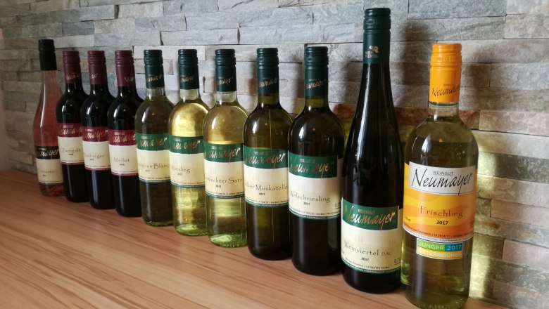 A row of wine bottles from the Neumayer winery in front of a stone wall.