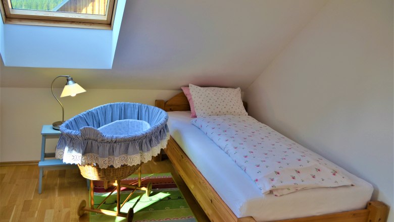 A cozy bedroom with single bed, baby cradle and skylight.