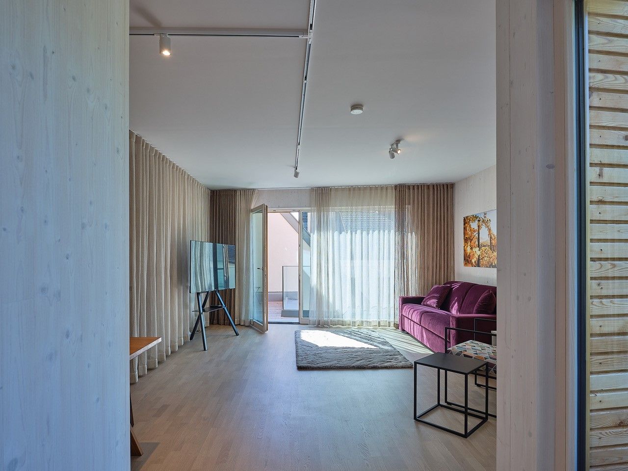 Modern living room with purple sofa, large window and TV on stand.