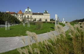Castle with green roof, surrounded by well-kept garden and walkway.