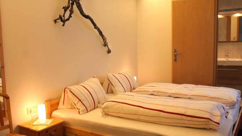 Cozy bedroom with double bed, bedside lamp and grapevine decoration on the wall.