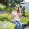 Woman sits in the garden and pours juice into a glass.