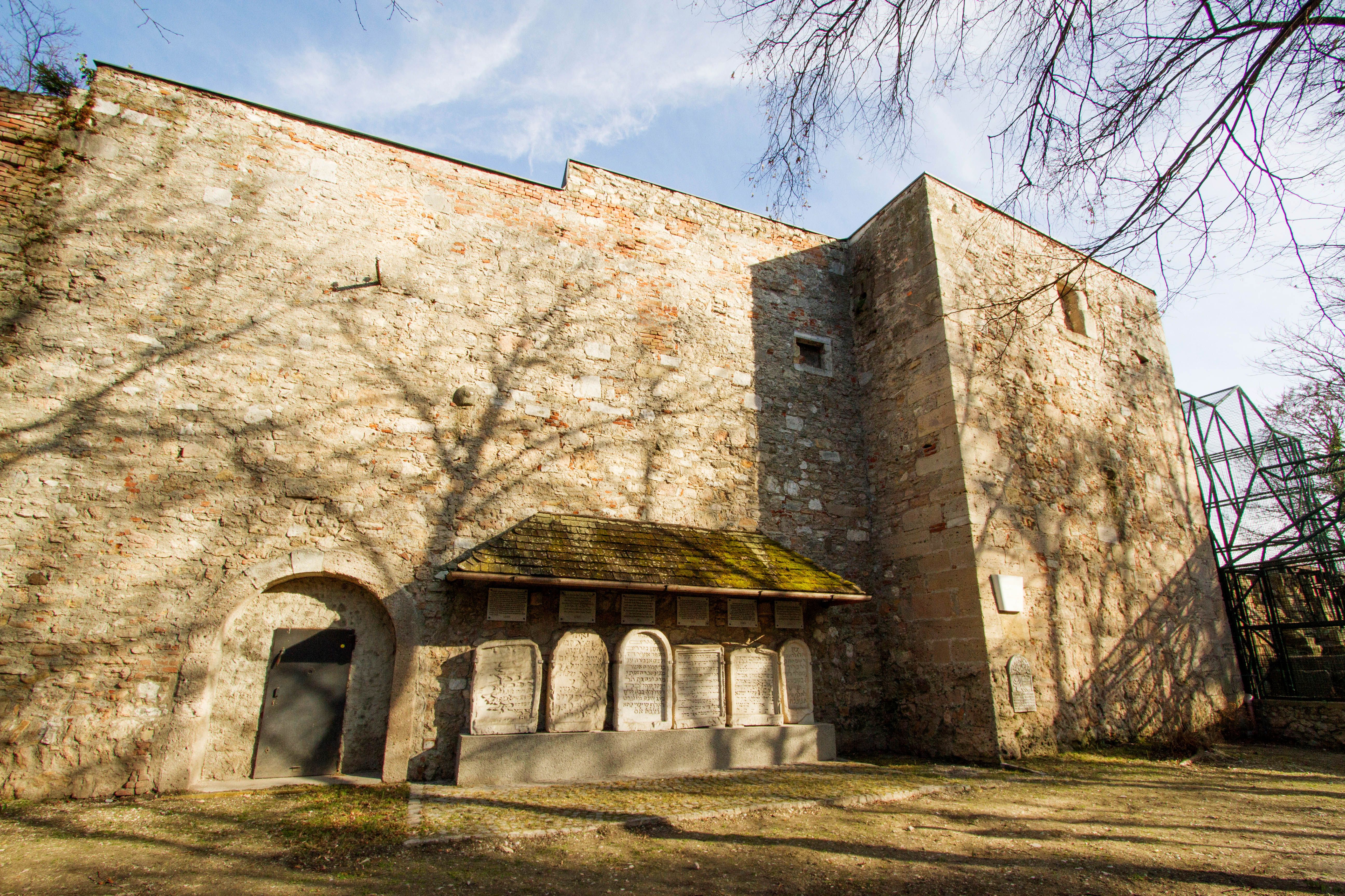 Stone wall with archway and memorial plaques, shade from trees on the wall.