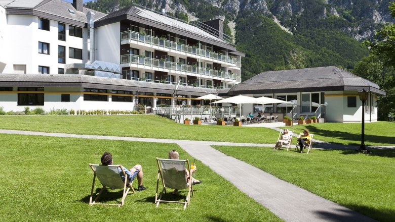 Parkhotel Hirschwang with deckchairs on a green meadow and mountains in the background.
