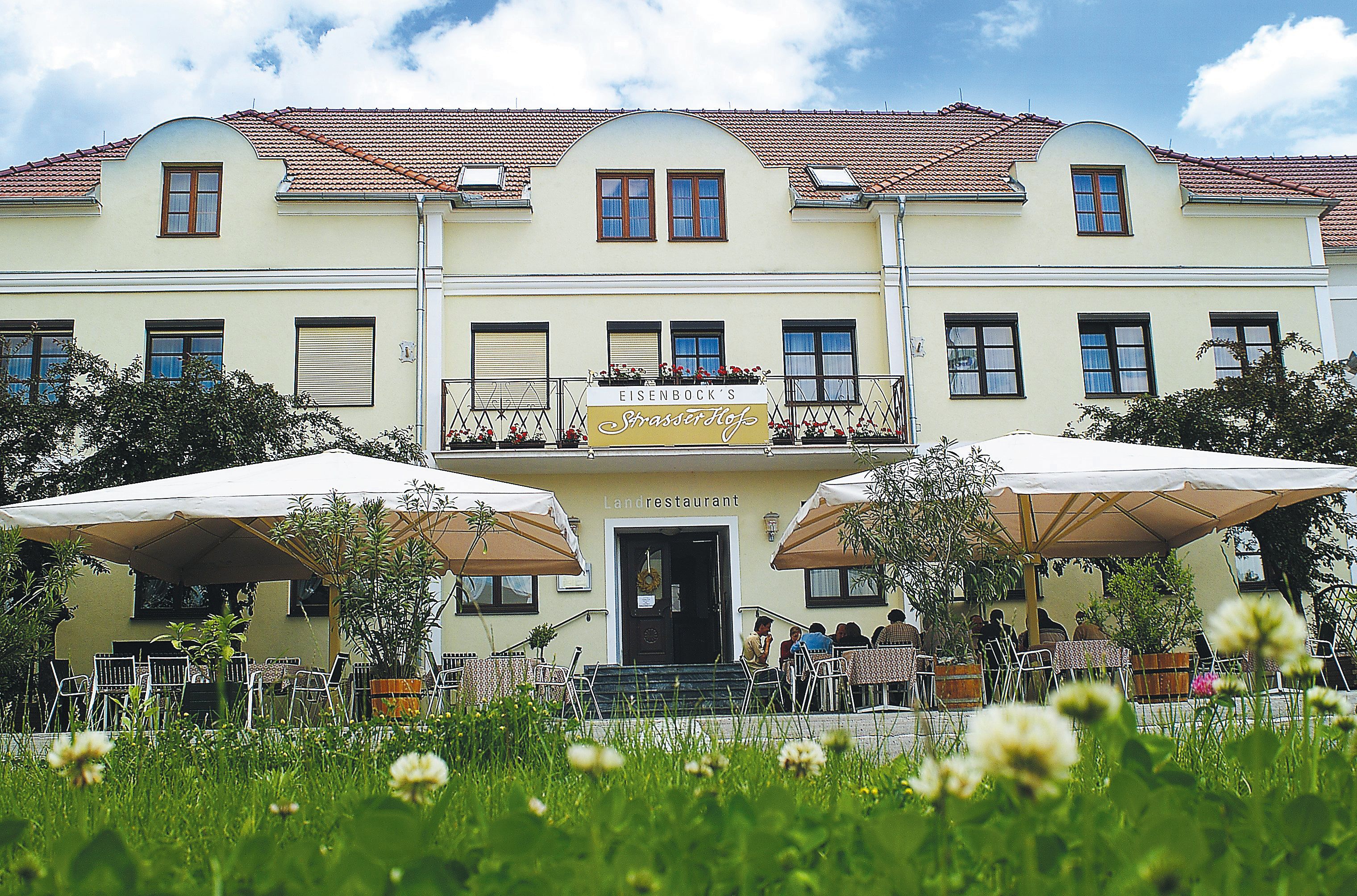 Exterior view of a yellow building with terrace and parasols.