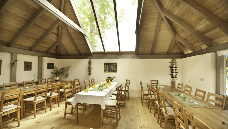 Interior view of a rustic room with wooden tables and chairs, a large skylight and decorative plants.