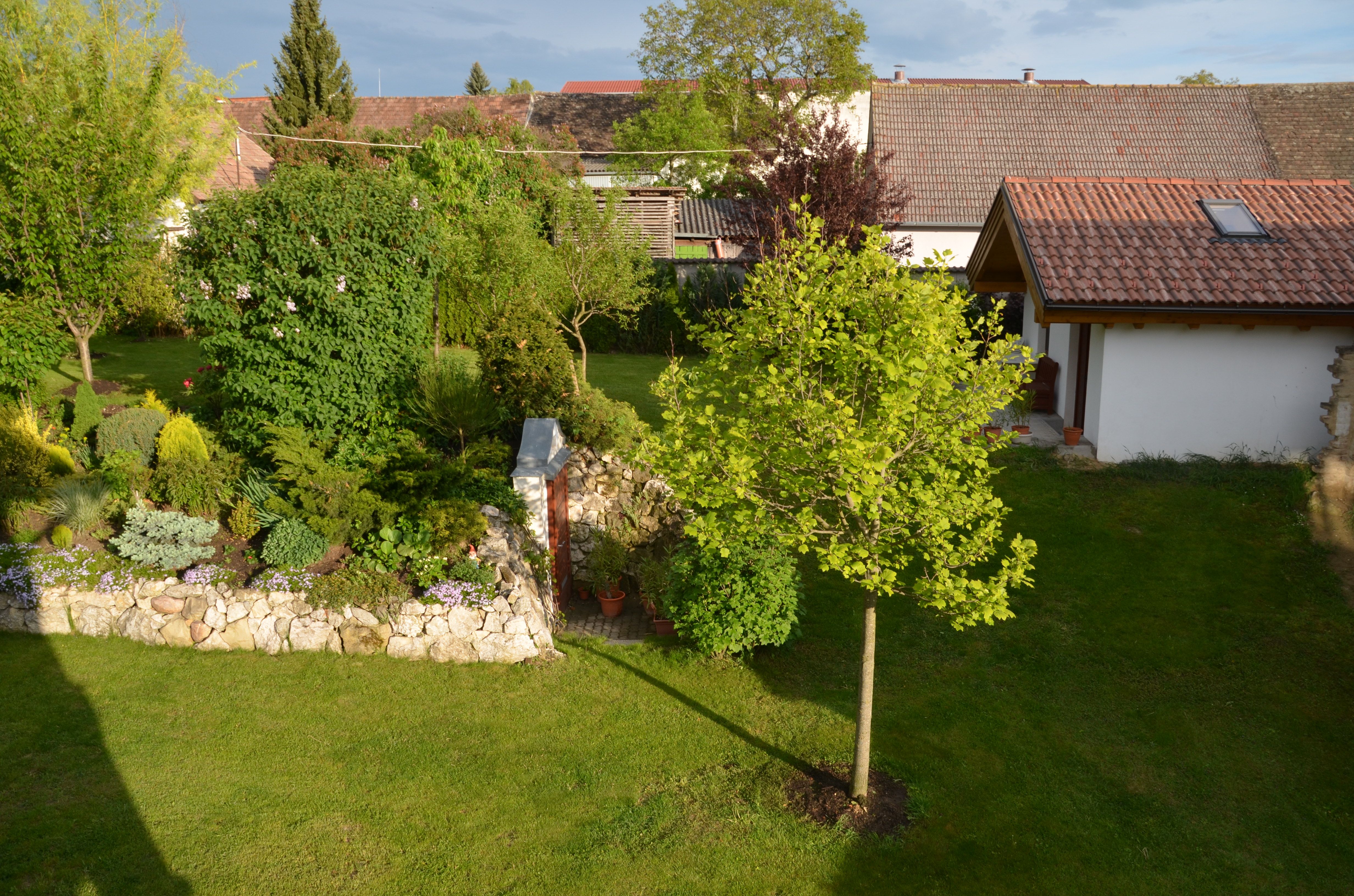 A well-kept garden with trees, shrubs and a small building with a tiled roof.