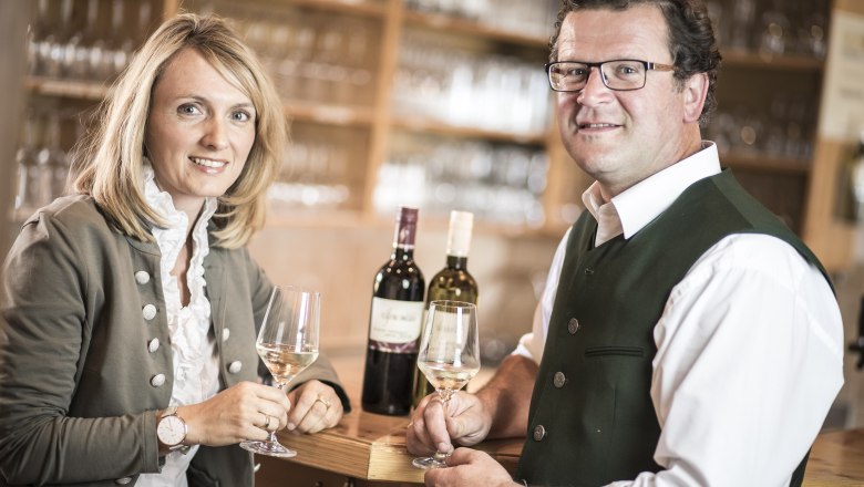 Two people in traditional dress holding wine glasses in a wine tavern.