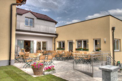 A cozy outdoor area with wooden tables and chairs in front of a yellow building.
