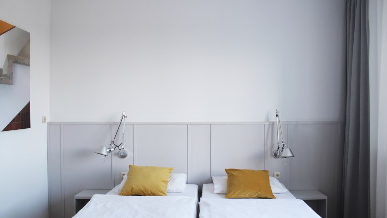 Guest room, © Stadthotel Hollabrunn Modern guest room with two single beds, yellow cushions and wall lamps.