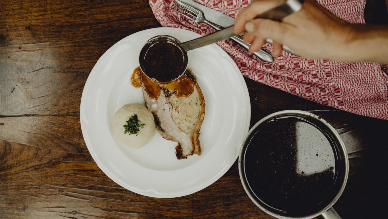 A plate of caraway roast and potato dumplings, covered in gravy, on a wooden table.