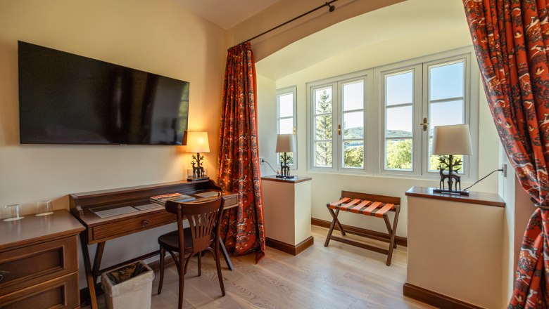 Hotel room with desk, chair, TV and window with a view.
