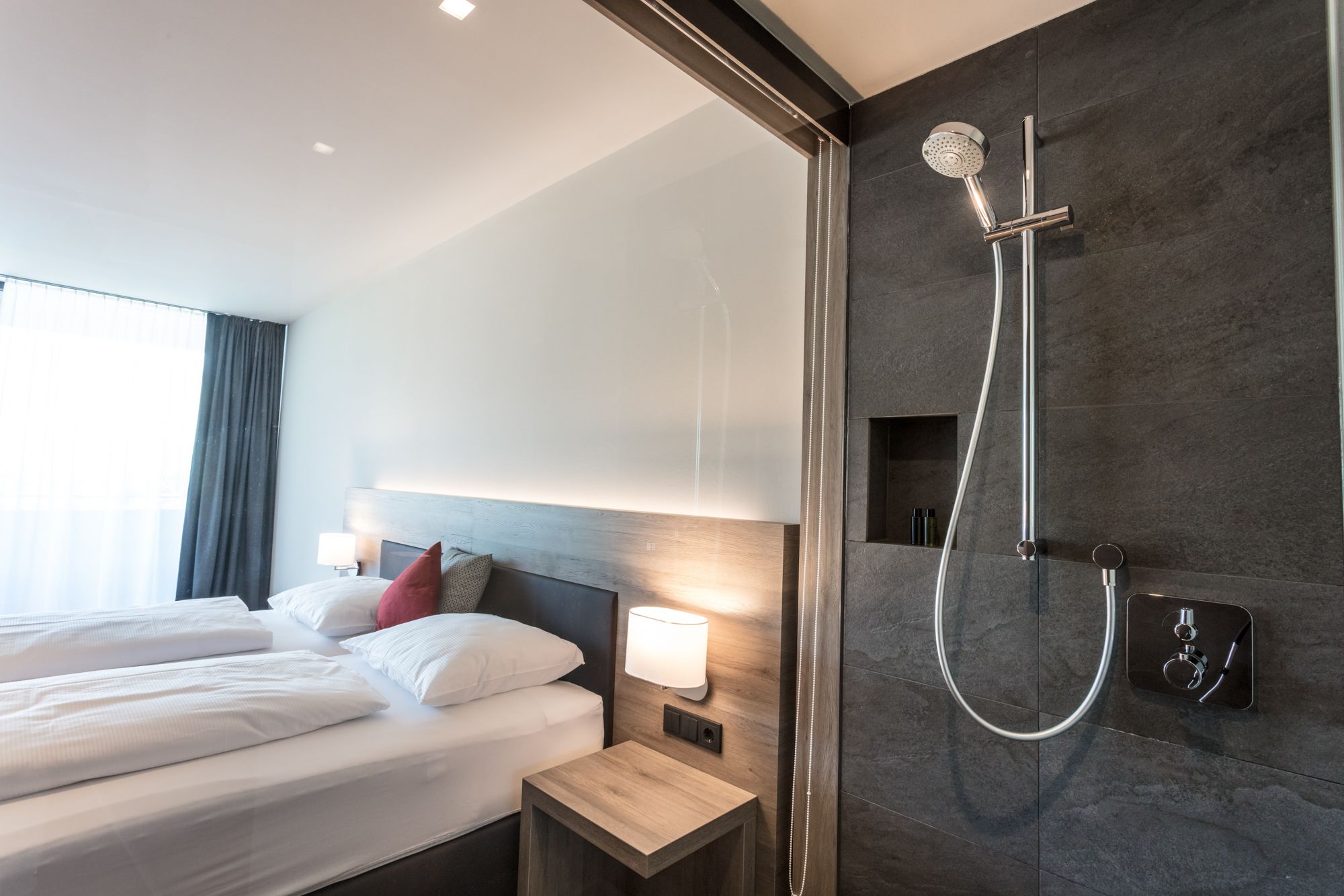 Modern hotel room with double bed and open shower.