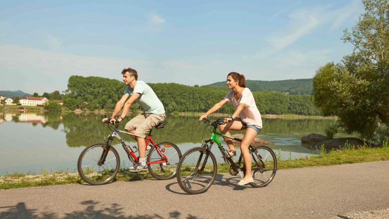 Two cyclists ride on a path along a river in the Nibelungengau.