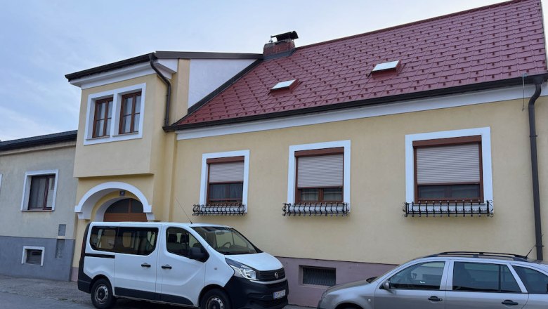 Two cars parked in front of a yellow house with a red roof.