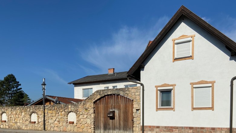 A white house with brown window frames and a stone wall with a wooden gate under a blue sky.