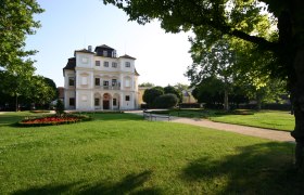 The Belvedereschlössl in Stockerau, surrounded by a well-tended garden with trees and flowerbeds.