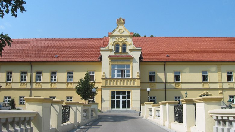 Young Hotel Tulln, © Junges Hotel Tulln Yellow building with a red roof and decorative façade, surrounded by a bridge and trees.