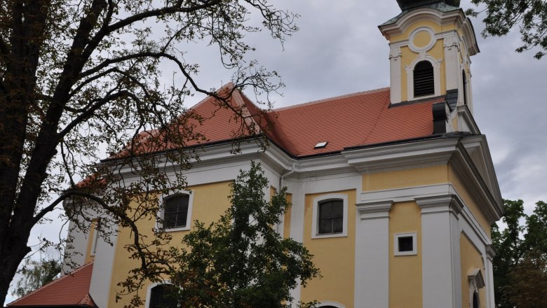 Yellow church with red roof and tower, surrounded by trees.
