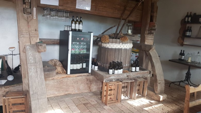 Interior view of a rustic wine bar with wine bottles, glasses and a fridge.